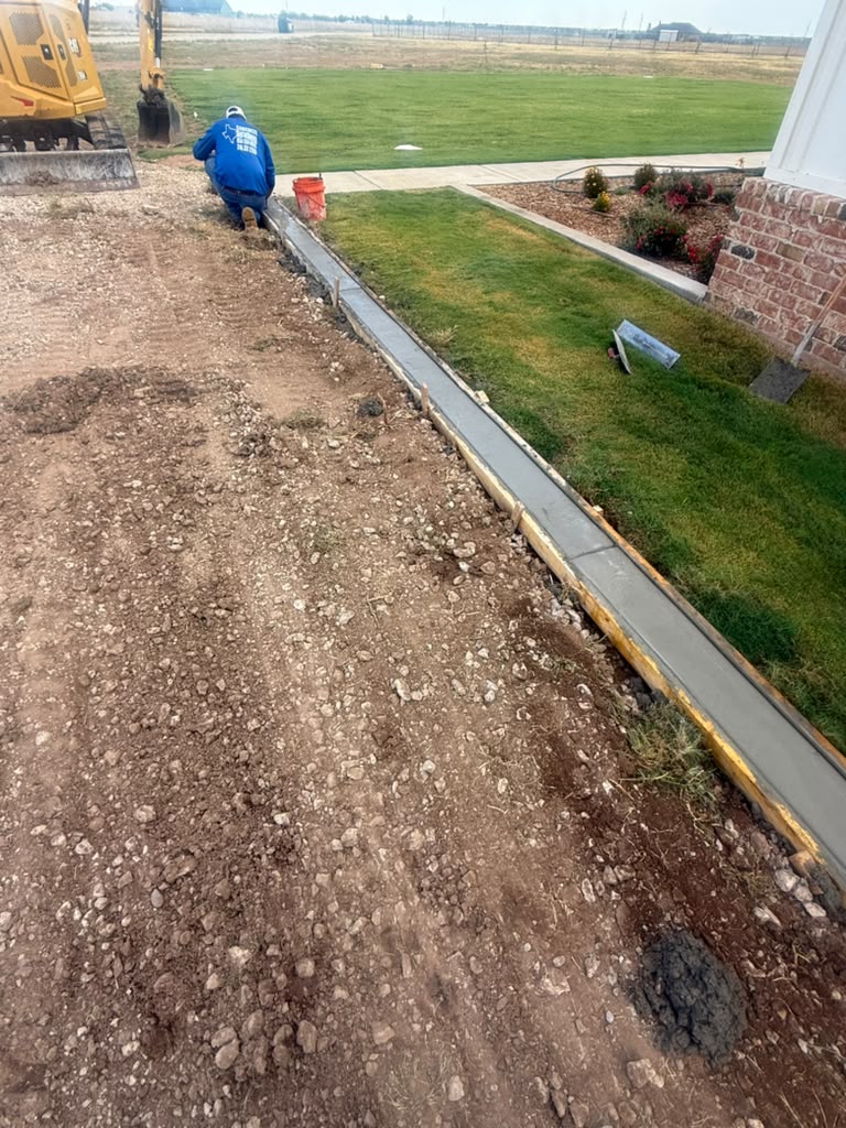 Crew finishing a straight concrete curb alongside the lawn.