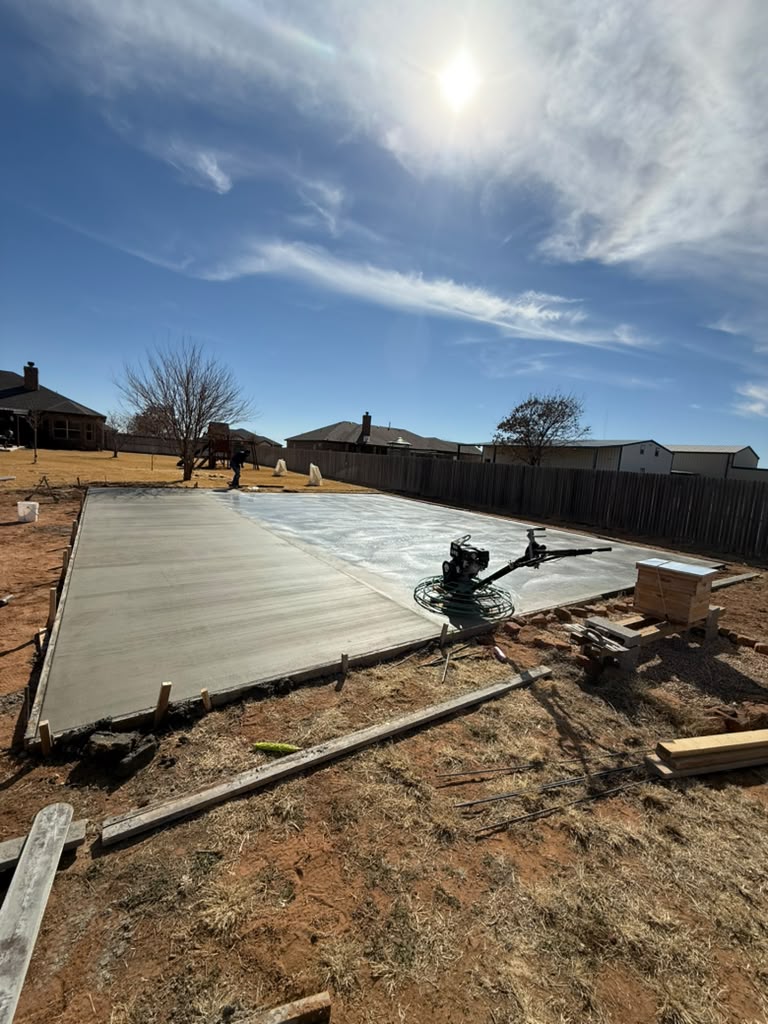 A broad concrete slab during finishing, with forms still in place.