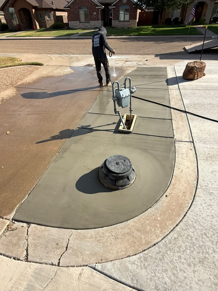 Fresh concrete fitted around existing utility fixtures beside a driveway.