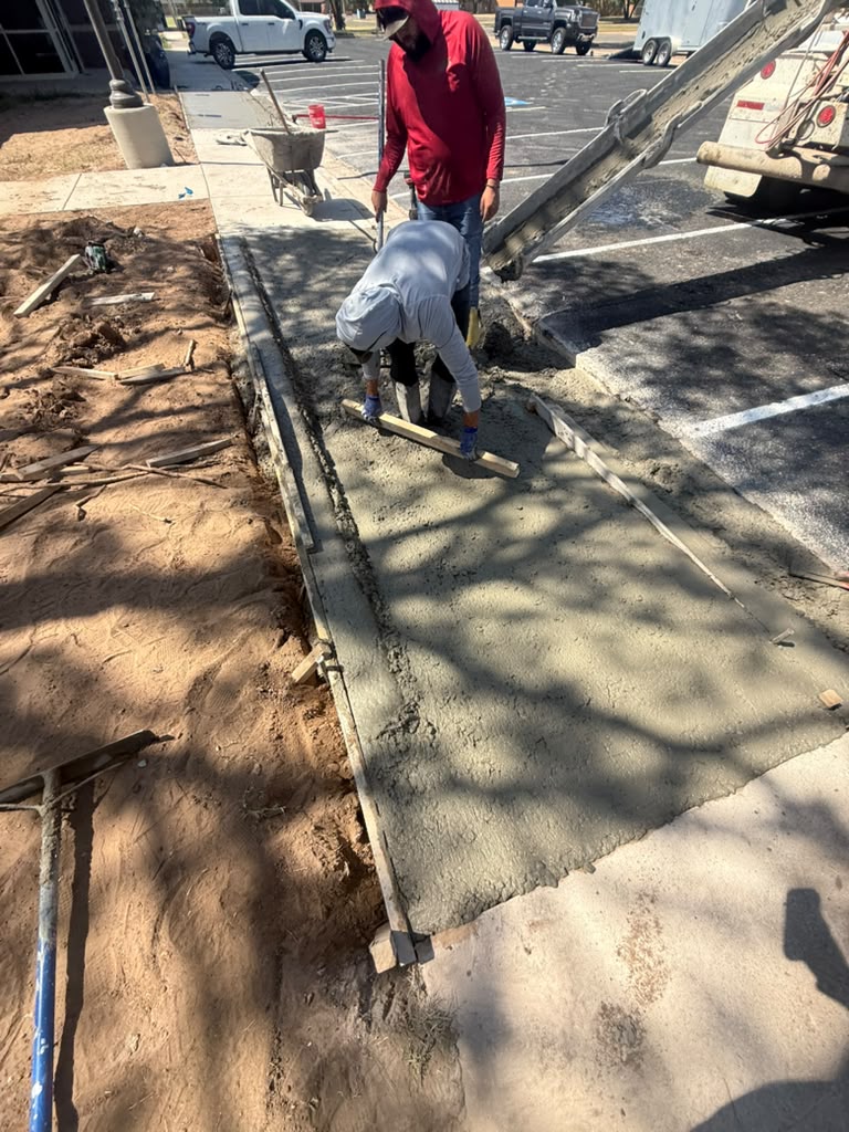 Crew screeding a new pour alongside a striped parking lot, pump truck on site.
