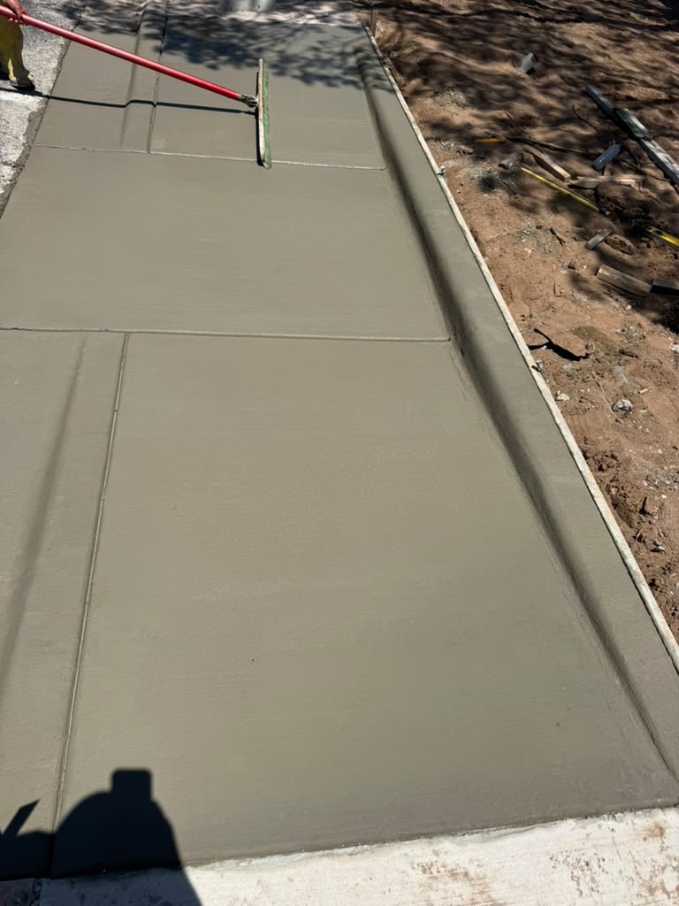 Broom finishing a fresh concrete apron beside a raised curb.